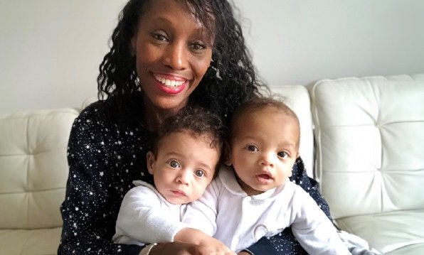 A black woman smiles at the camera holding twin babies on her lap