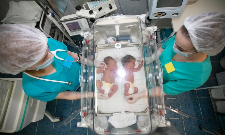 An overhead view of a neonatal bed with twin babies being cared for by two people in scrubs