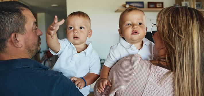 A man and a woman stand with their backs to the camera, each holding a toddler facing the camera
