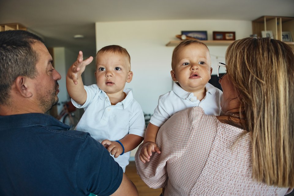 A man and a woman stand with their backs to the camera, each holding a toddler facing the camera
