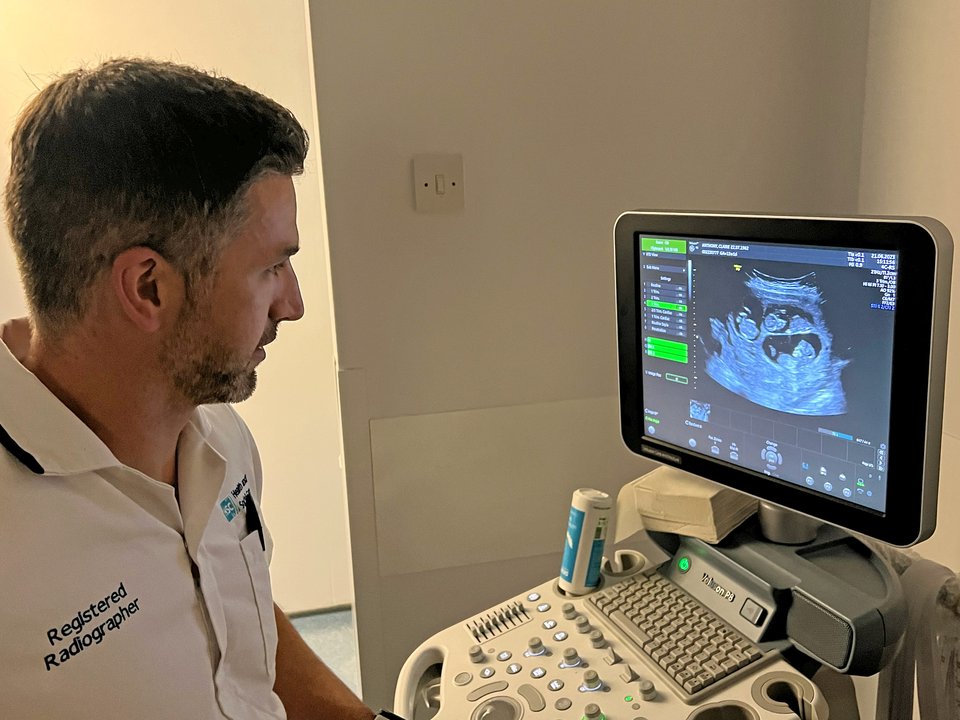 A man wearing a shirt with the words Registered Radiographer looks at a sonography screen