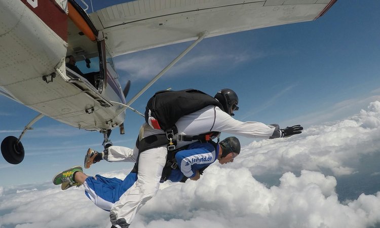 two people skydiving in tandem jumping off a plane in the sky