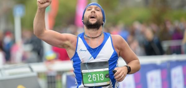 male runner wearing vest with scottish flag raising his right fist in celebration while running