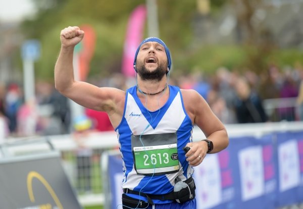 male runner wearing vest with scottish flag raising his right fist in celebration while running